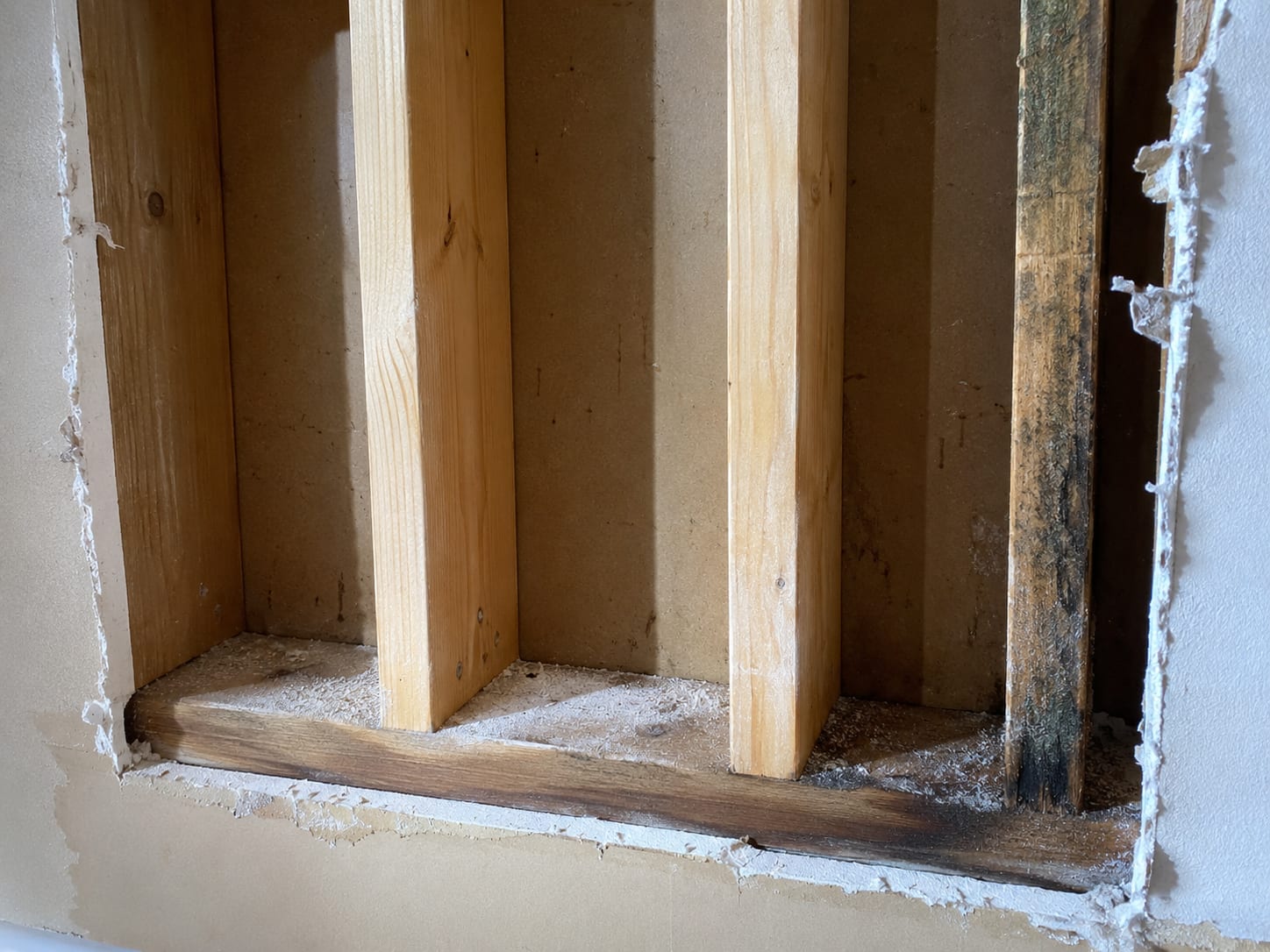 Close-up of an opened interior wall cavity in a New Jersey home showing removed drywall with cleaned and treated wall stud framing, residual dark staining contrast visible between original and remediated wood surfaces