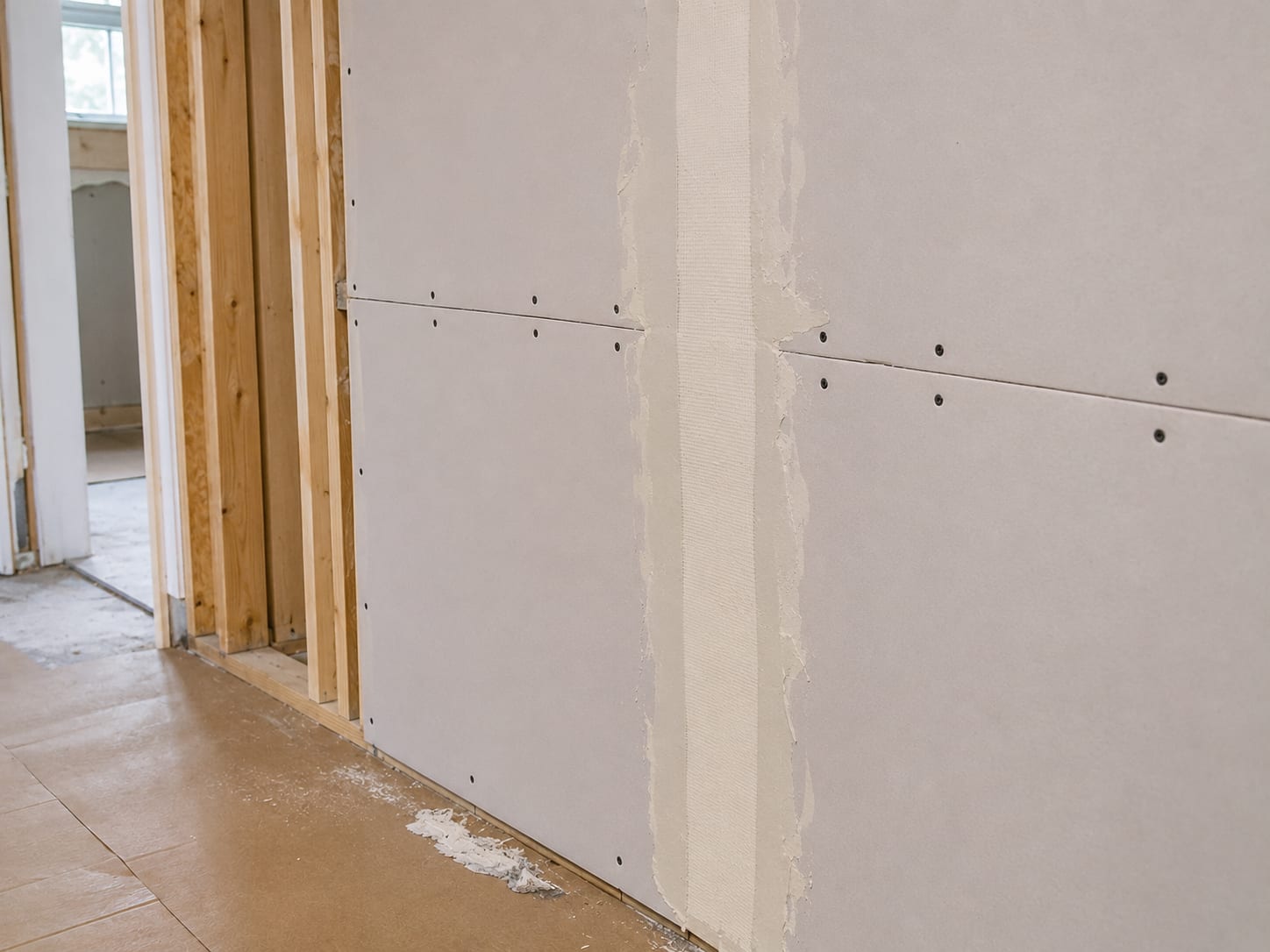 Close-up of freshly installed drywall panels being screwed and taped on a bare wall stud frame inside a New Jersey home during build-back reconstruction