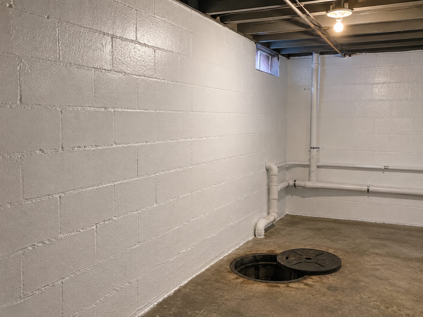 Post-remediation treated commercial basement mechanical room showing freshly encapsulated concrete block walls coated in white antimicrobial paint beside a sump pit and PVC drainage pipes