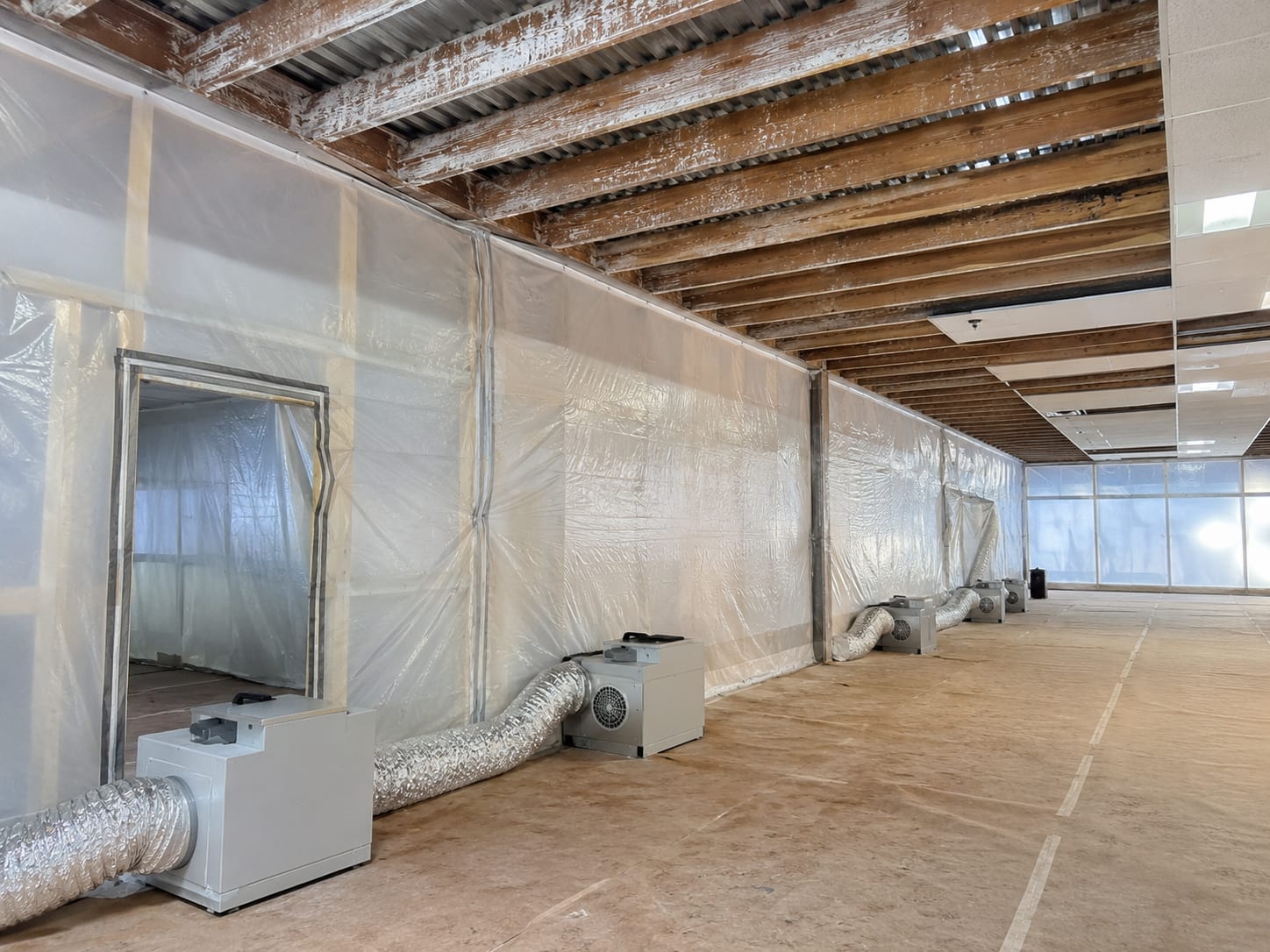 Wide view of a commercial building interior under full mold remediation containment with polyethylene sheeting barriers and HEPA negative air machines