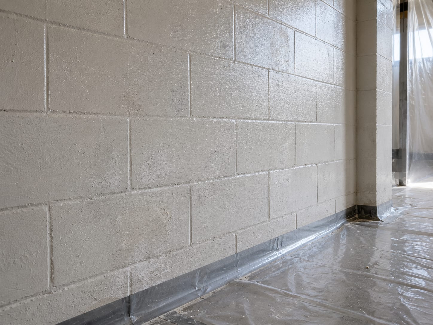 Close view of a commercial building concrete block wall after mold remediation showing clean dry surface with faint antimicrobial treatment residue and sealed containment sheeting on the floor