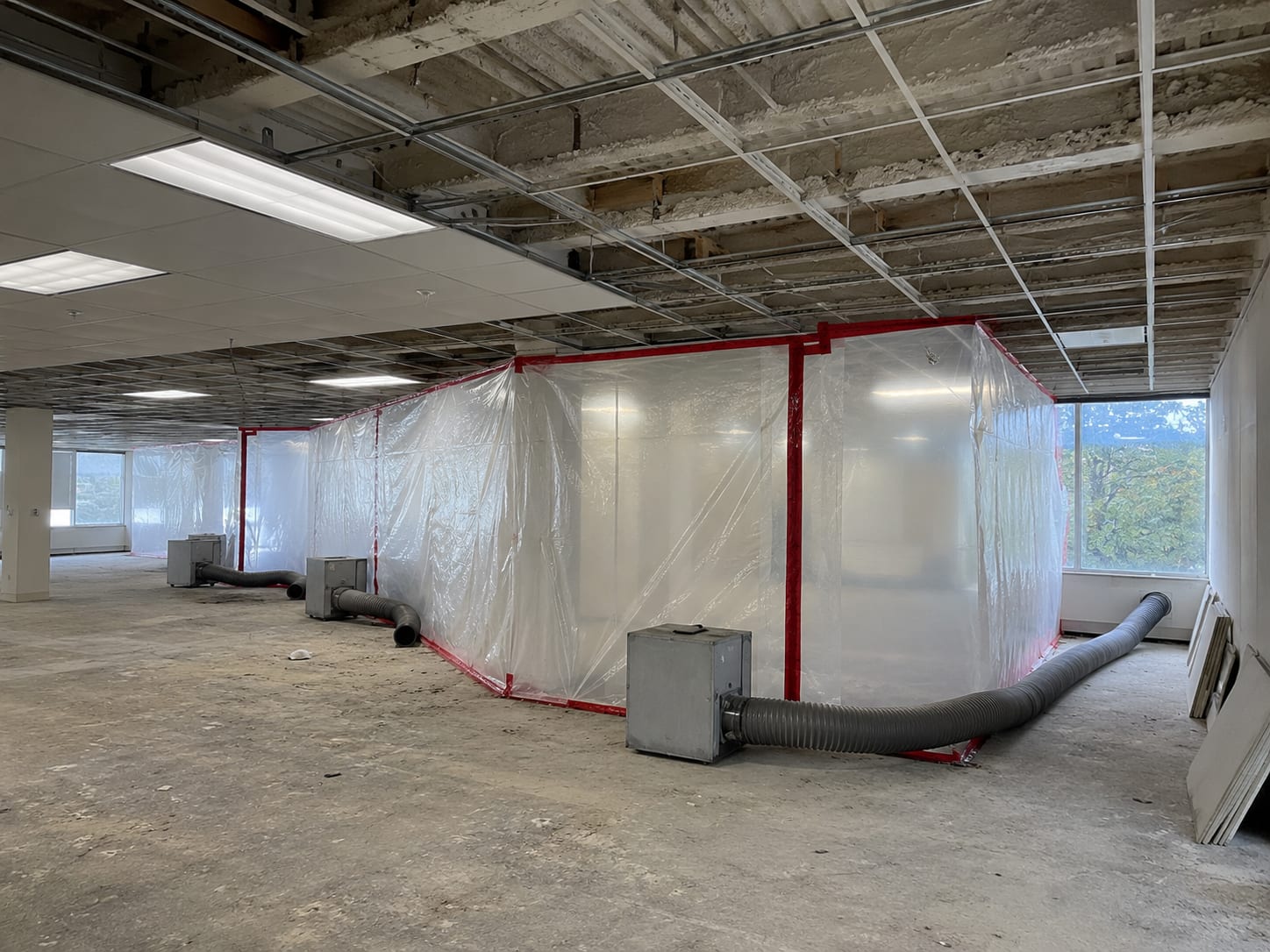 Wide view of a commercial office building interior under active mold remediation containment with heavy-duty plastic sheeting and negative-air scrubbers