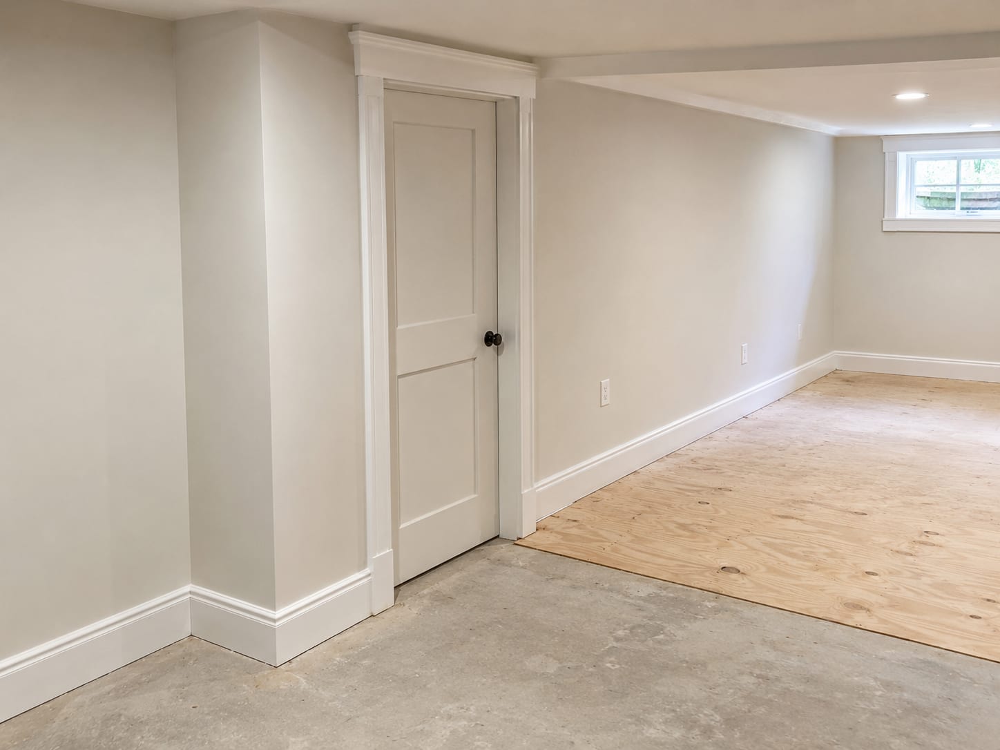 Freshly rebuilt basement finishing with custom-fitted trim, new drywall panels, and painted wood casing around a utility doorway in a New Jersey home