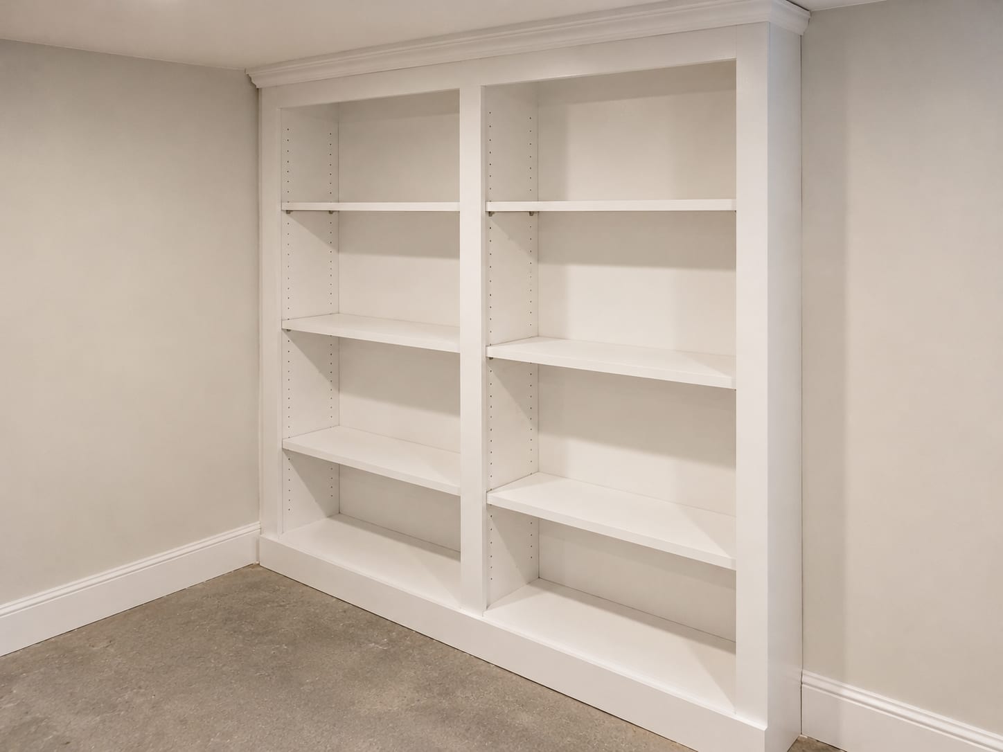 Newly built white-painted custom shelving unit with adjustable shelves installed against a smooth drywall wall in a restored New Jersey basement utility or storage room
