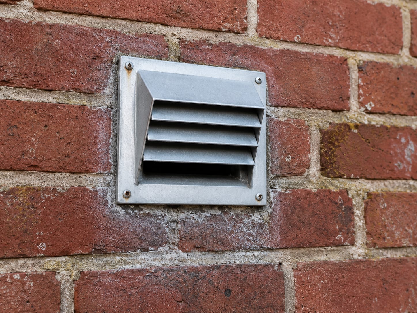 Close view of a clean exterior dryer vent cap mounted on a brick house wall with no lint obstruction visible