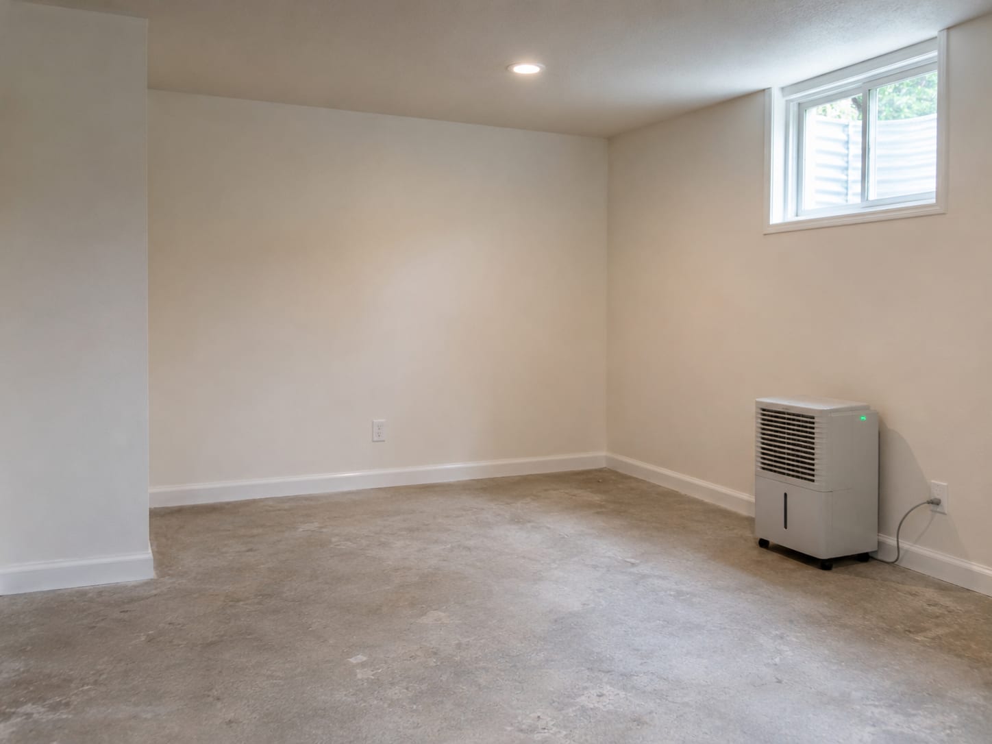 Clean newly painted basement room with fresh drywall installation and dehumidifier running beside a window after completed mold remediation