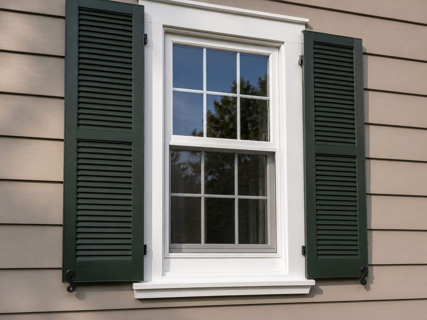 Freshly painted dark green shutters and white window trim on a cape cod home exterior in natural daylight