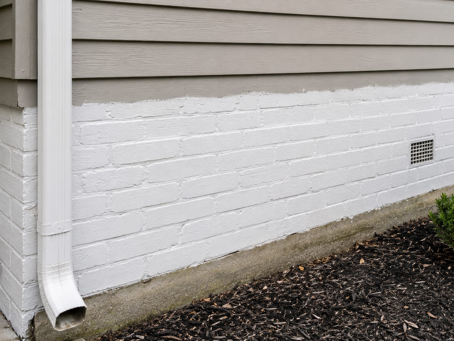 Freshly painted white brick foundation wall with masonry paint on the lower section of a New Jersey residential home exterior