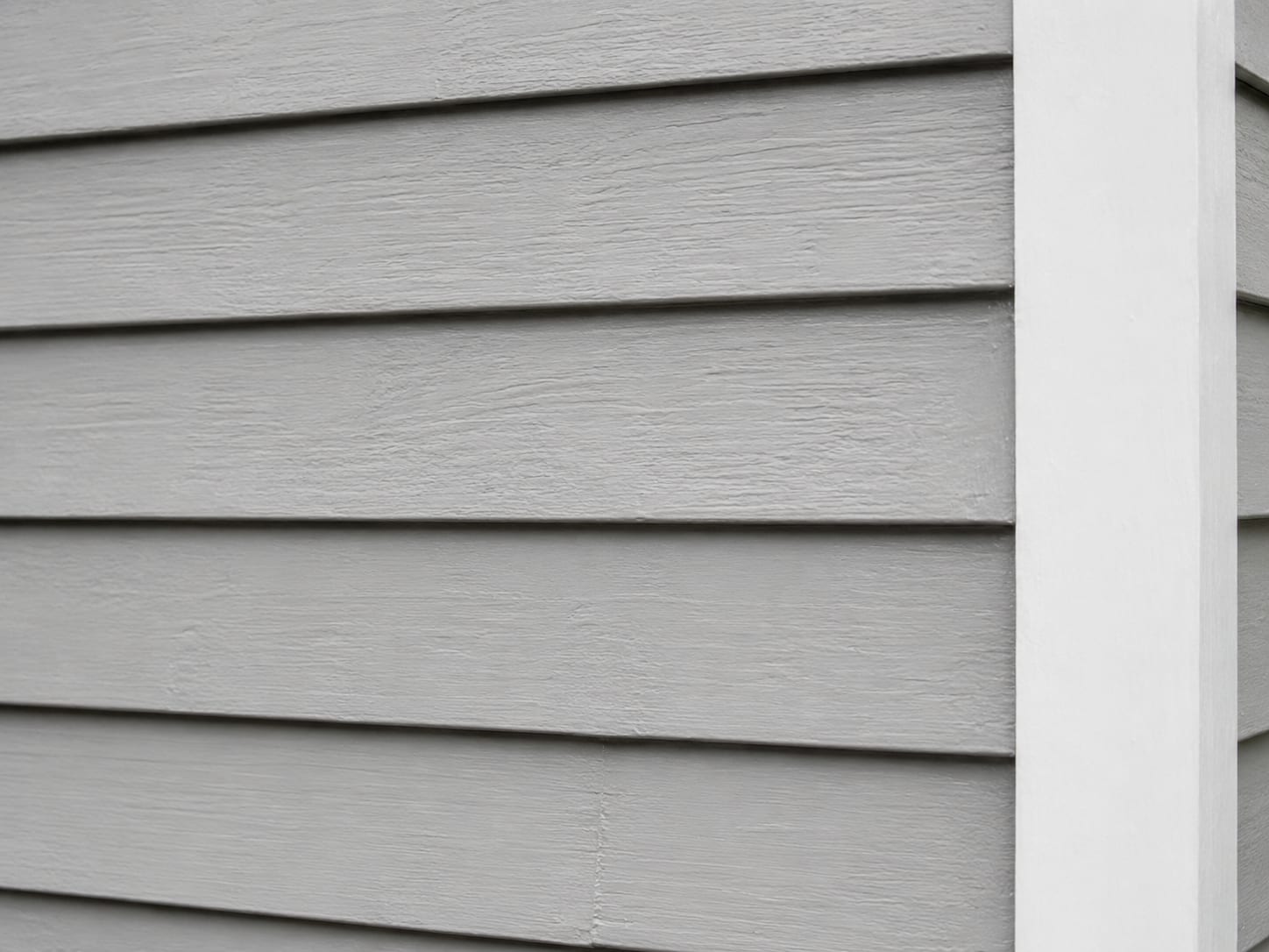 Close-up of freshly painted light gray clapboard siding with crisp white trim edge on a residential home exterior