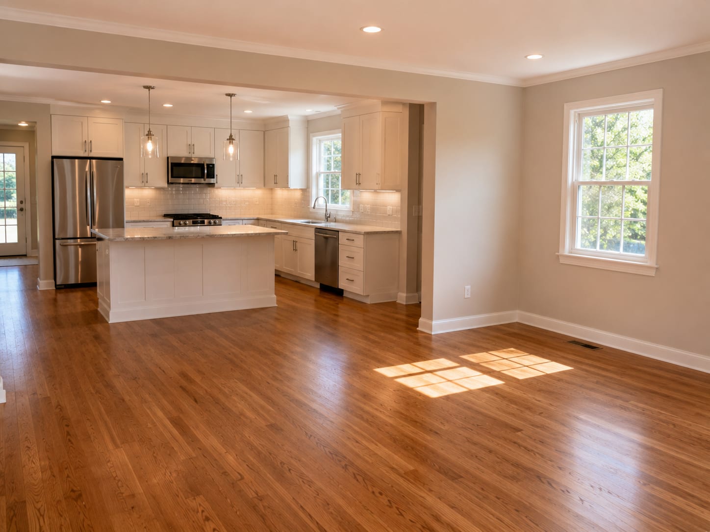 Bright open-plan kitchen and adjacent living area in a fully remodeled New Jersey colonial home showing new cabinetry, hardwood floors, and natural light flooding through a double-hung window