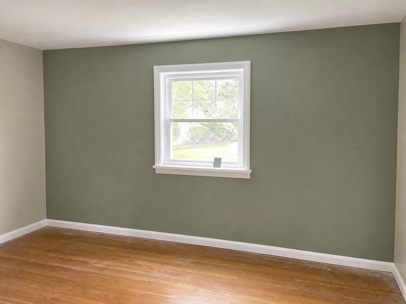 Freshly painted bedroom in a mid-century New Jersey home with crisp white painted window trim and casings against a warm sage green accent wall, hardwood floor visible
