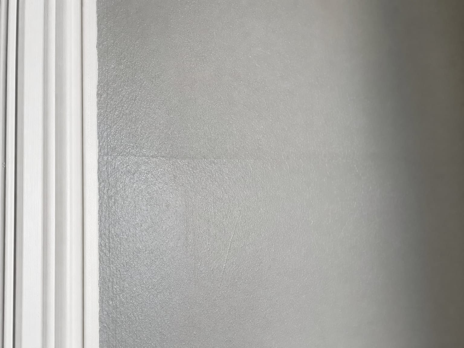 Close-up of a freshly painted drywall surface in soft gray showing roller stipple texture and a crisply cut painted corner where wall meets white trim