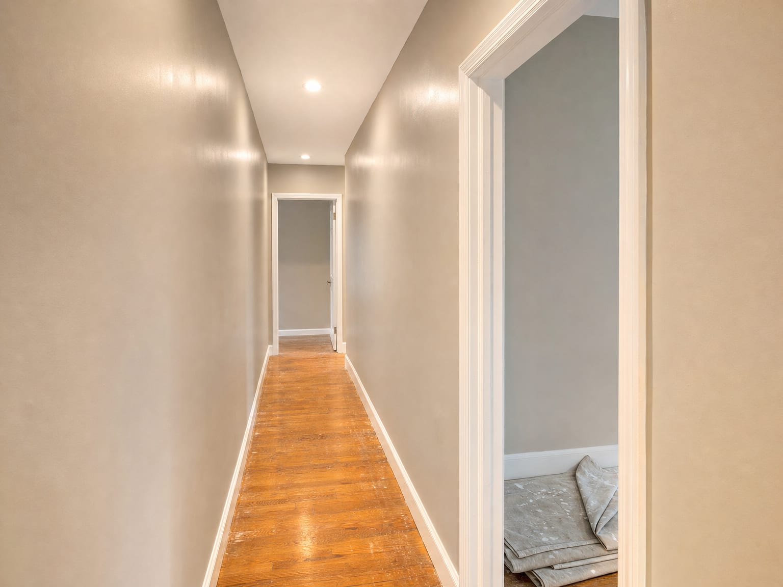 Freshly repainted narrow hallway in a New Jersey colonial home with bright white ceiling and warm greige walls, painted door frames visible at each end