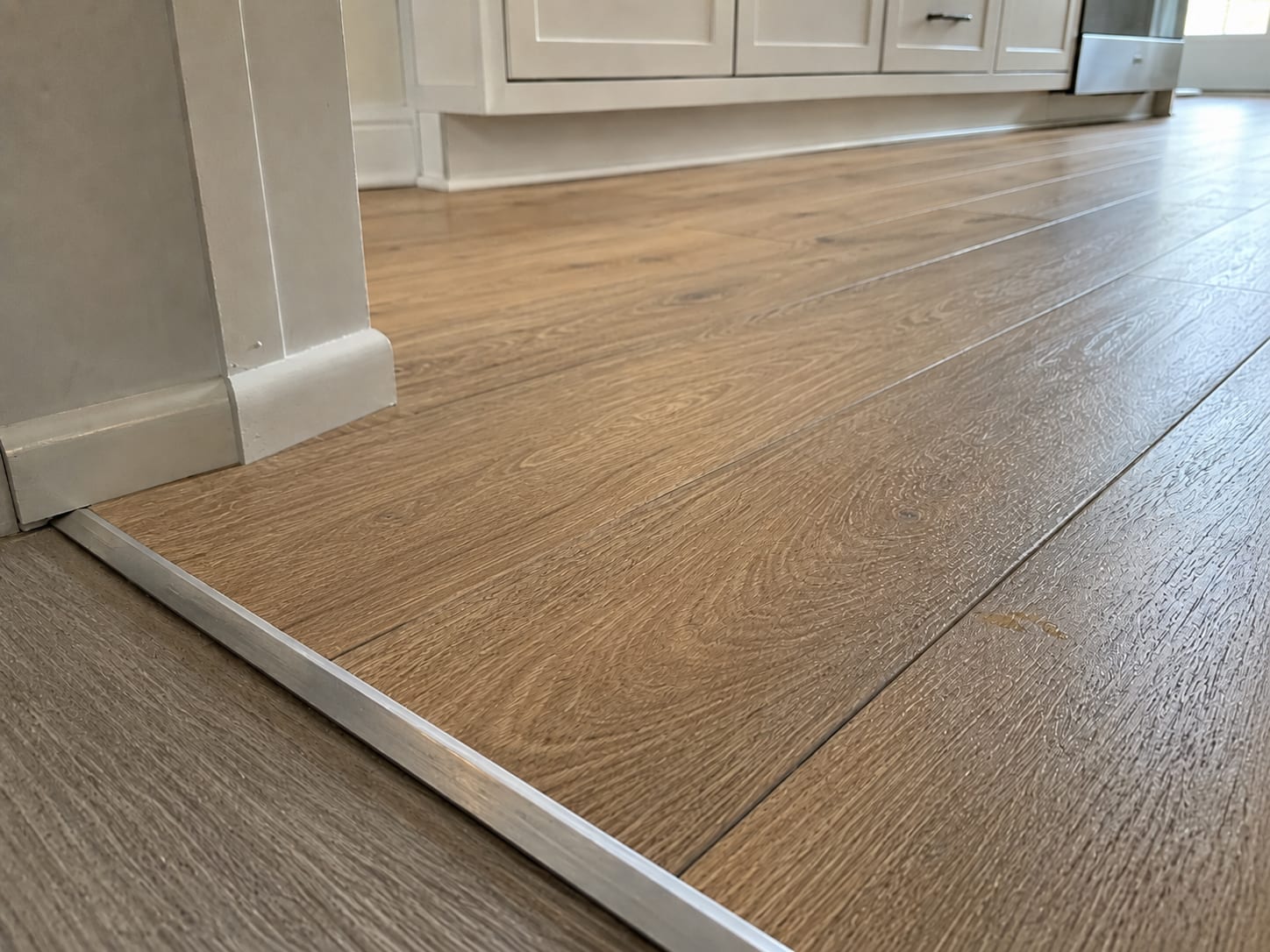 Freshly installed luxury vinyl plank flooring in a renovated New Jersey kitchen showing the floor surface running to a doorway transition strip and base molding