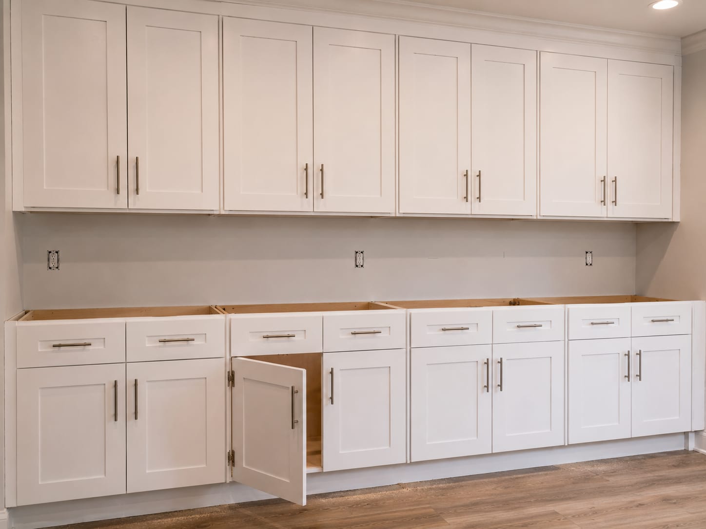 Row of freshly installed white shaker cabinet doors with brushed-nickel pulls along a kitchen wall, showing even reveals and new hinges in a New Jersey home renovation