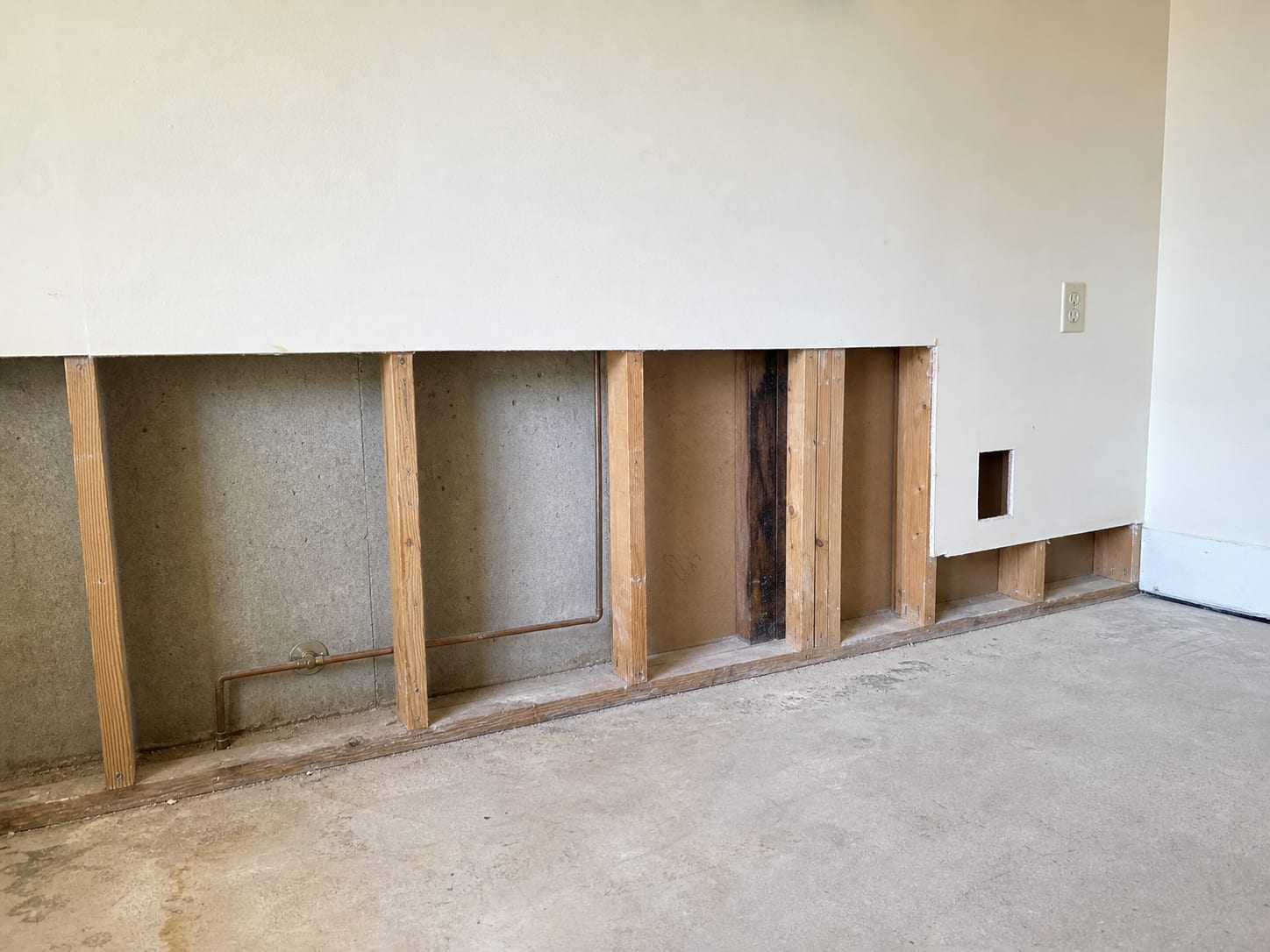 An interior wall opened to the studs in a detached New Jersey home, with insulation removed, a small inspection opening cut lower down and the framing left exposed
