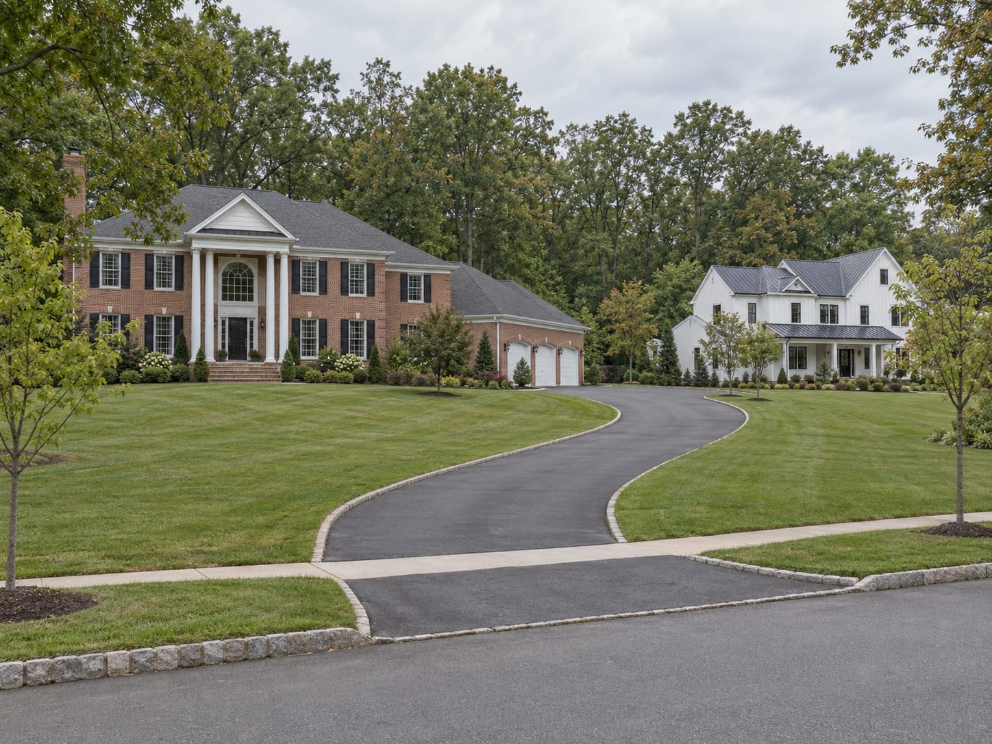 A large brick fronted colonial with a side load garage on a wide lawn backed by woods, beside a newer white board and batten house, in Belle Mead, New Jersey