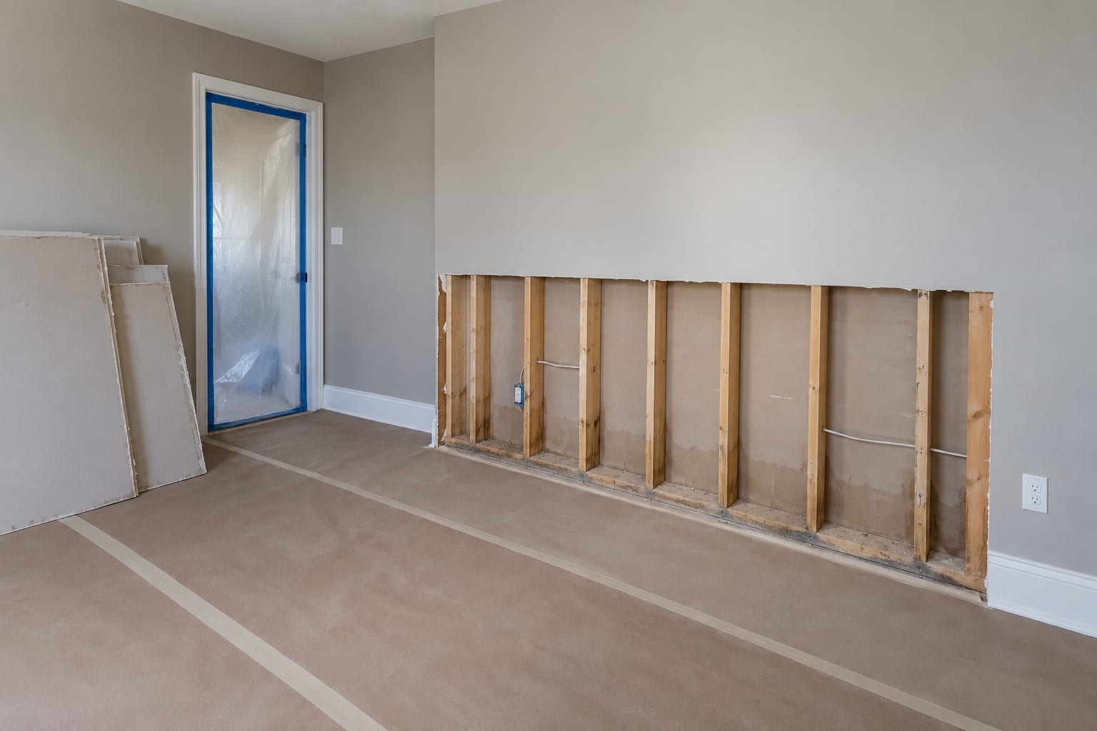 A bedroom wall cut open to bare studs with cleaned framing, beside an intact painted wall and a stack of cut drywall, in a Belle Mead, New Jersey house