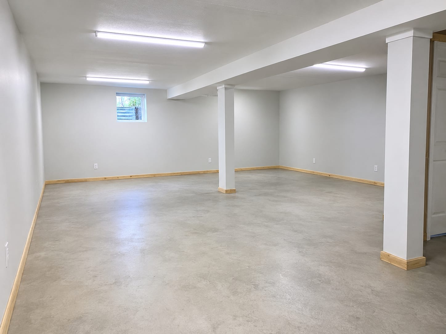 Freshly painted and rebuilt basement interior with new drywall, clean concrete floor, and bright overhead lighting after completed mold remediation work