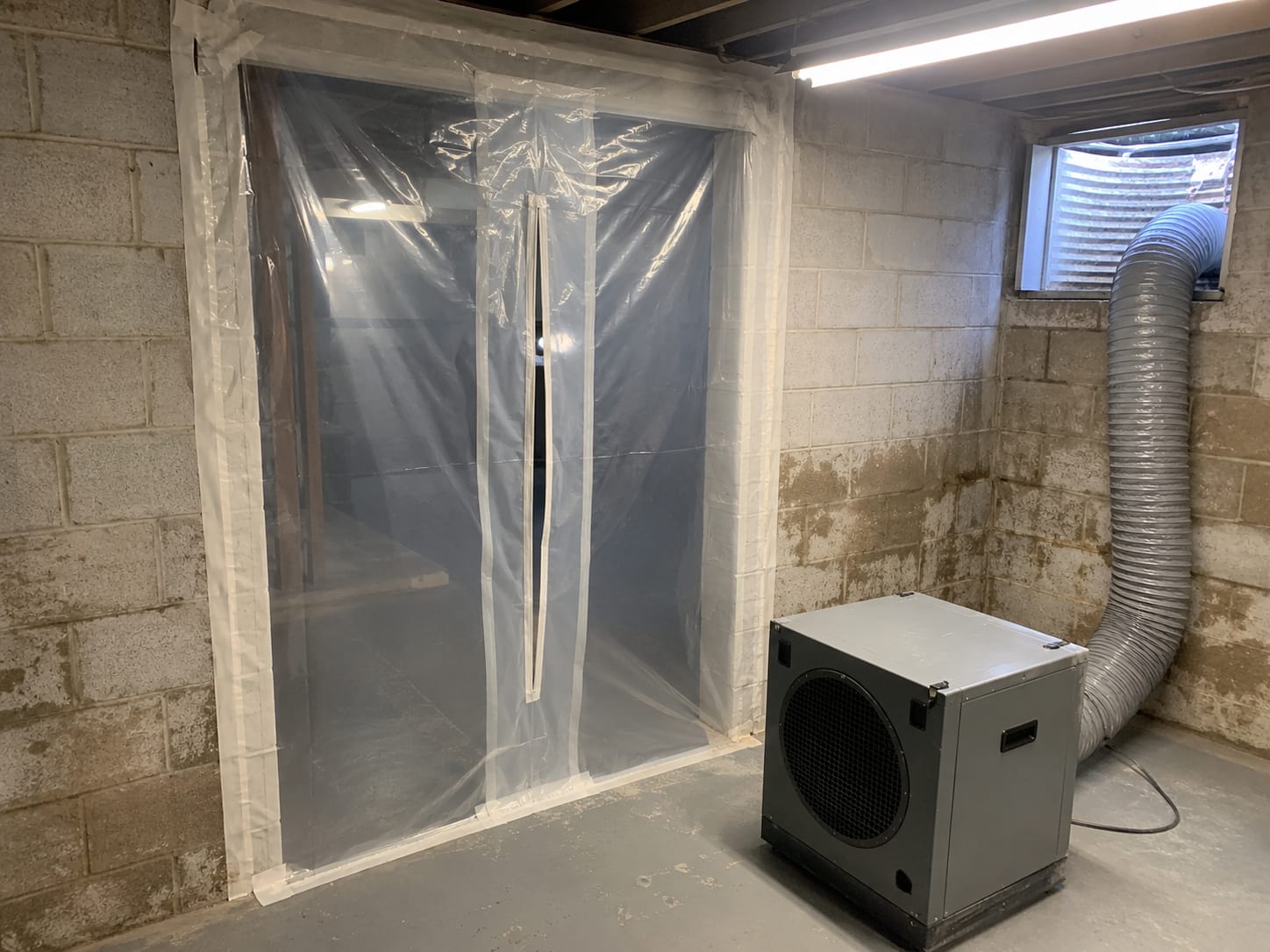 Plastic containment sheeting sealing a basement doorway with negative air machine visible