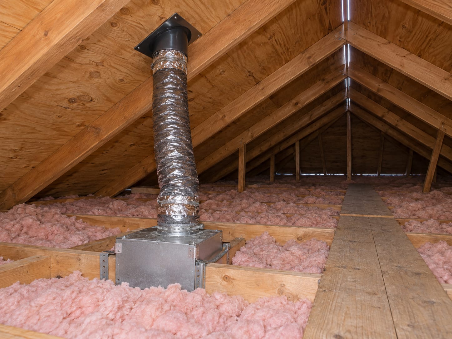A bathroom fan duct runs through a Dayton townhouse attic to a roof vent, over dry rafters and level insulation.