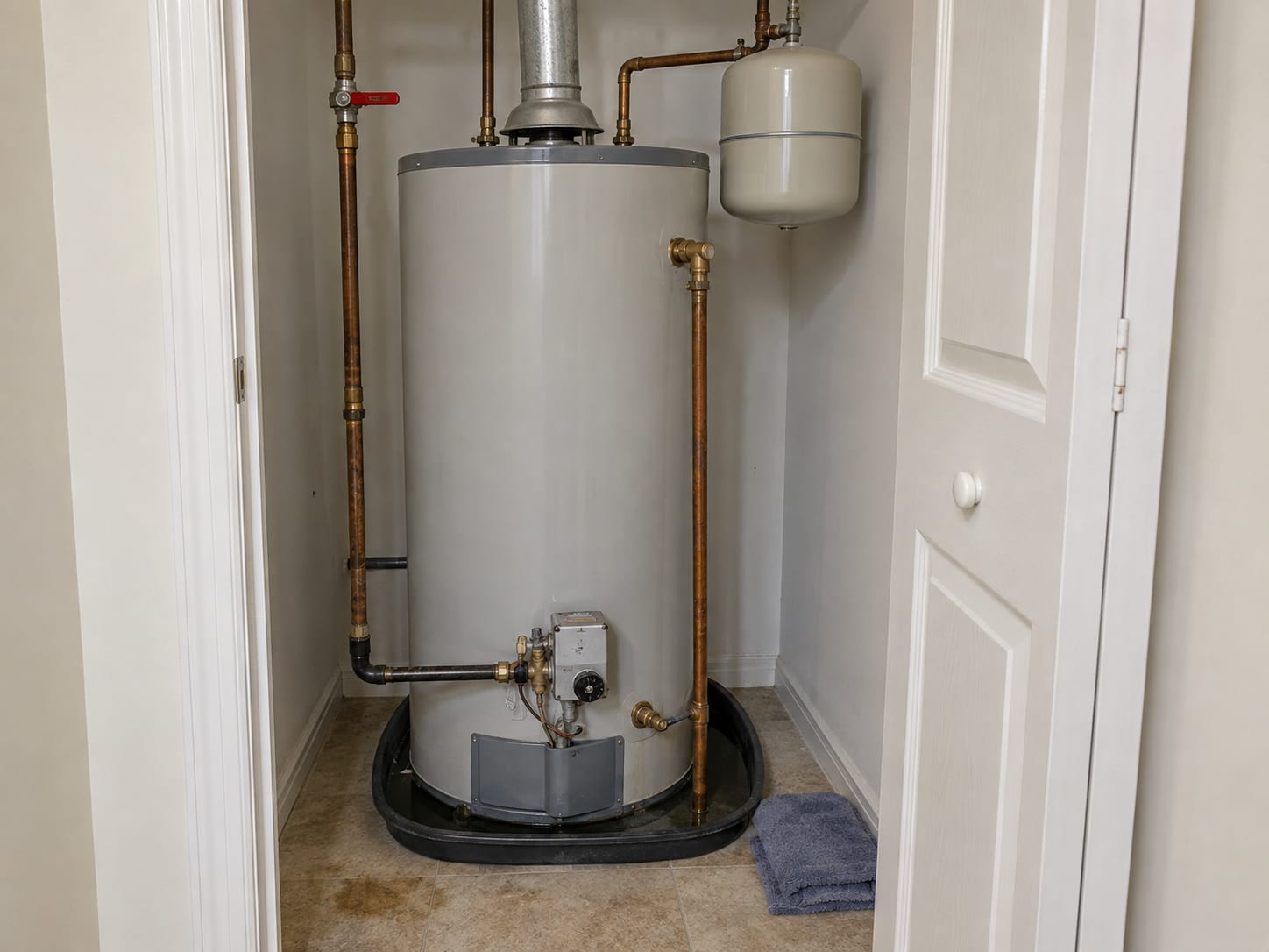 A water heater closet in a Dayton townhouse shows the closed cold supply valve and a damp drip pan beneath the tank.