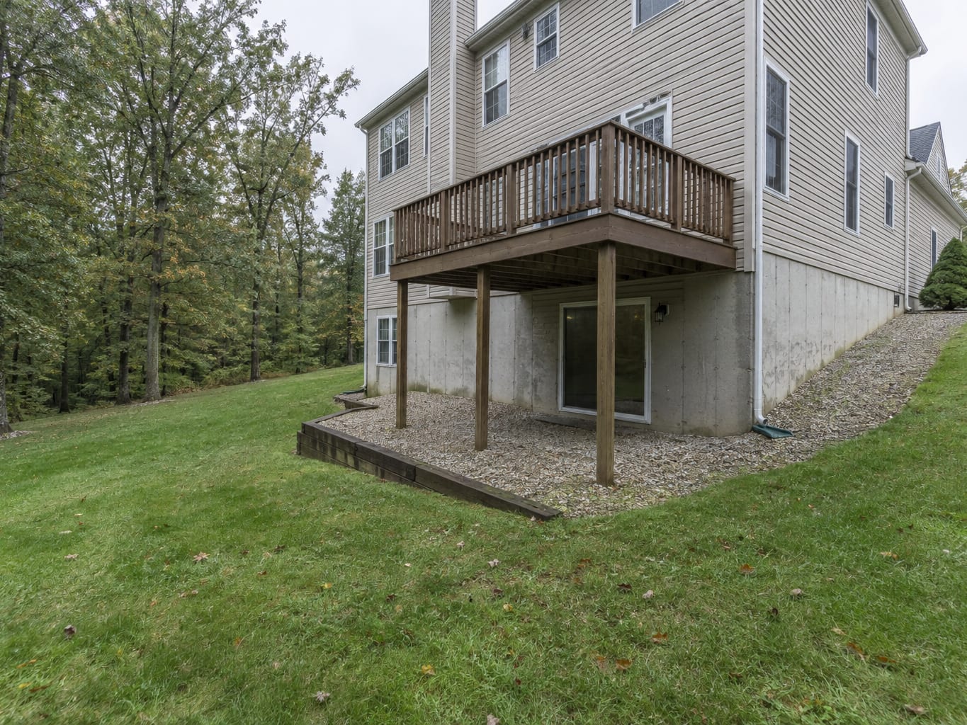The rear of an East Rocky Hill colonial shows a walkout basement door at grade and a wooded slope beyond the lawn.