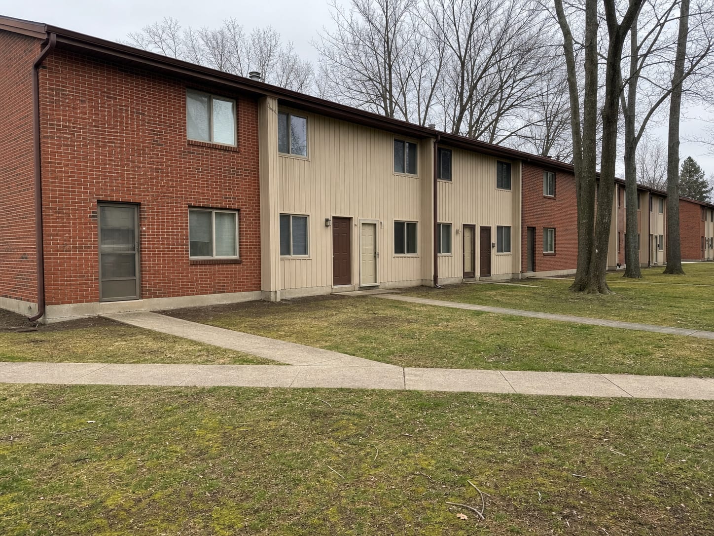 A row of 1970s attached townhomes on a common lawn in central New Jersey, with downspouts discharging at grade beside the slab foundations