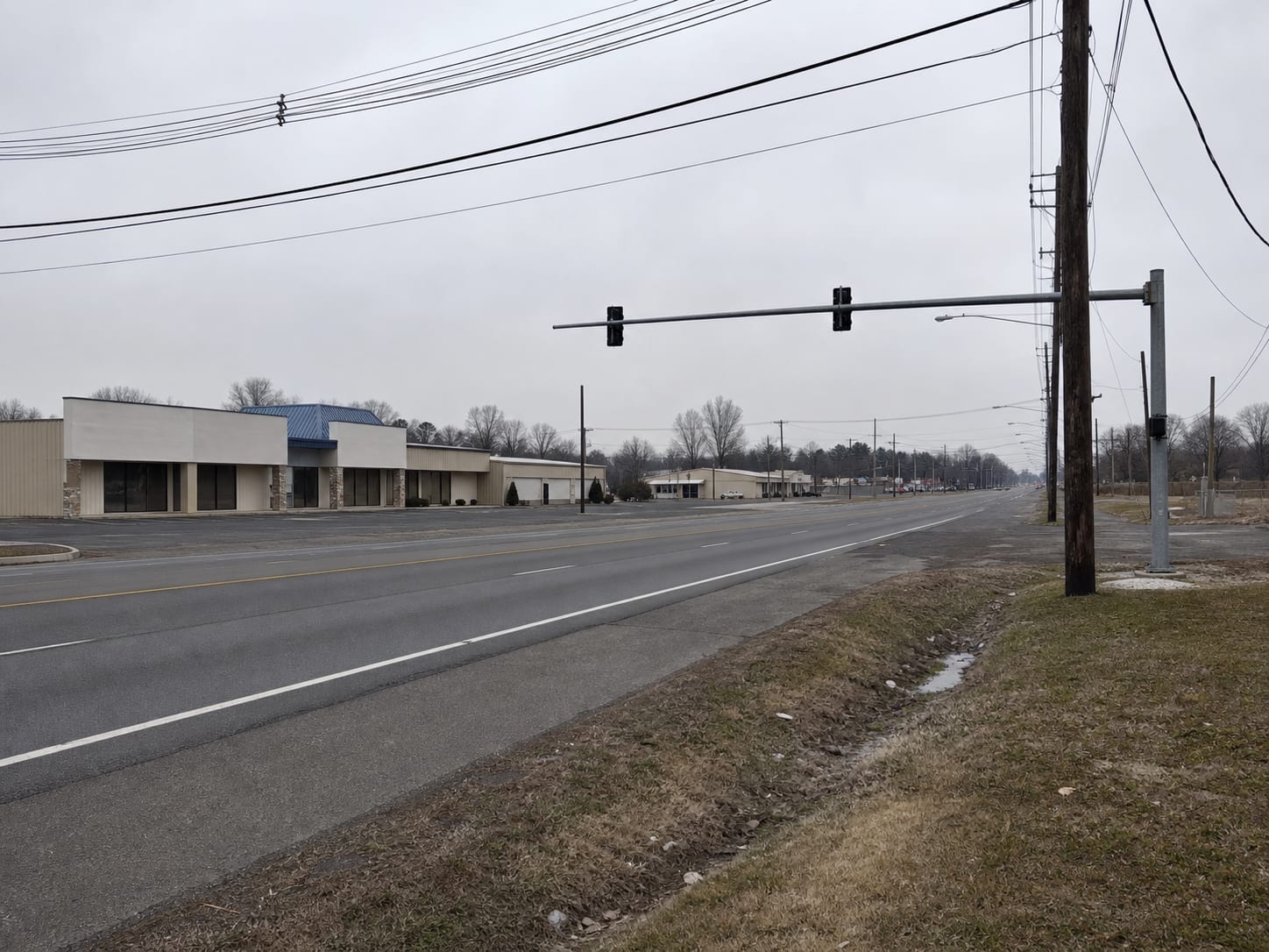 A low rise commercial corridor in inland central New Jersey with wide shoulders, utility poles and flat open farmland on the horizon