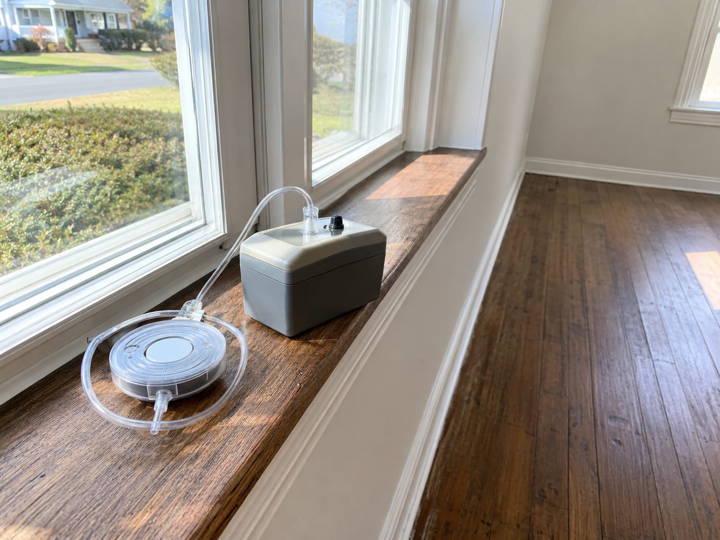 Air sampling pump with cassette attached sitting on a windowsill inside a clean residential room in New Jersey after mold remediation