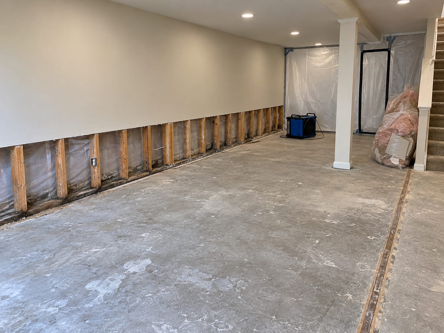A finished basement with the lower part of a drywall wall cut away in a straight line, wet insulation removed and bagged debris beside it, in a Forsgate, New Jersey home