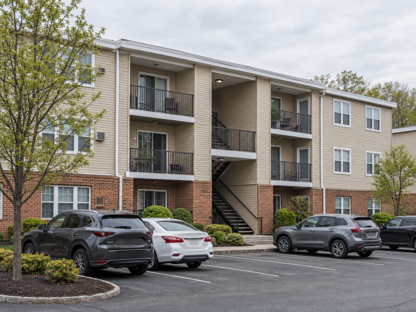 A three storey brick and vinyl garden apartment building with stacked balconies, breezeway stairs and a parking court, in Franklin Township, New Jersey