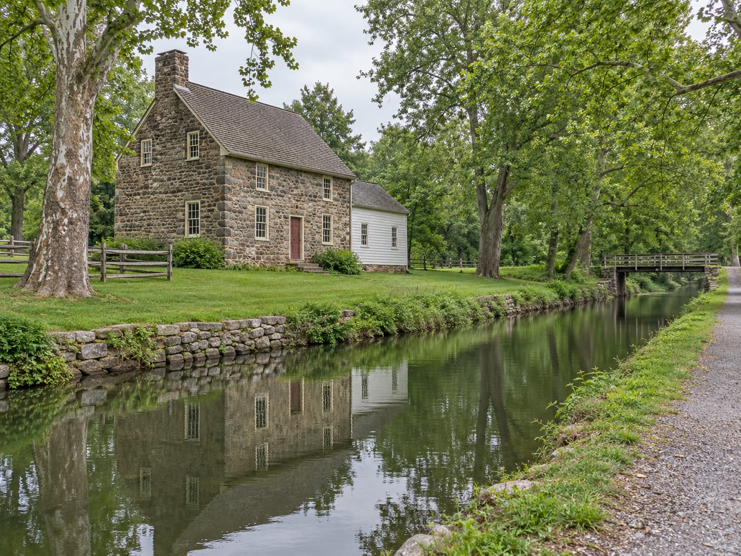 An old fieldstone house with a later frame addition and a stone foundation beside a still canal and a wooded towpath, in Franklin Township, New Jersey