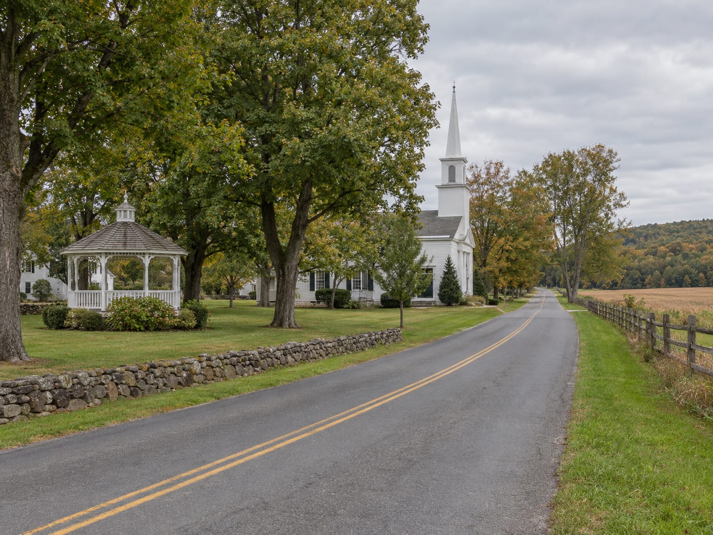 A rural road past a small village green with a white gazebo, a white clapboard church and preserved farmland behind a fence, near Harlingen, New Jersey