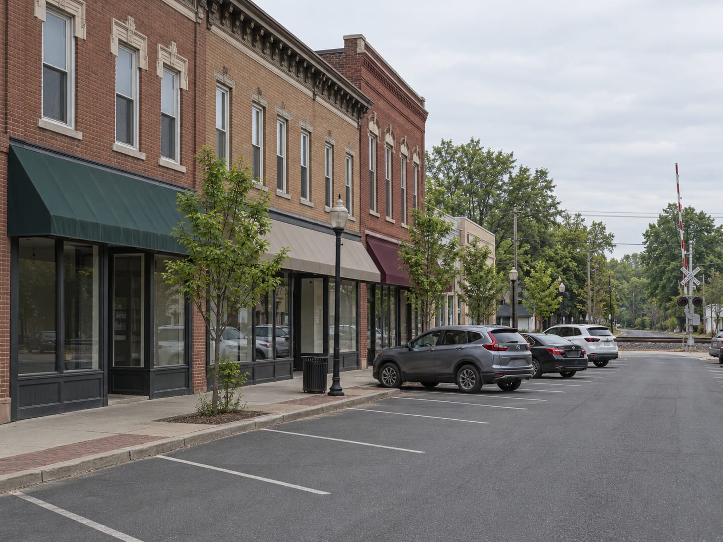 A small town street of two and three storey brick buildings with blank storefront windows, angled parking and a railroad crossing in the distance, in Jamesburg, New Jersey