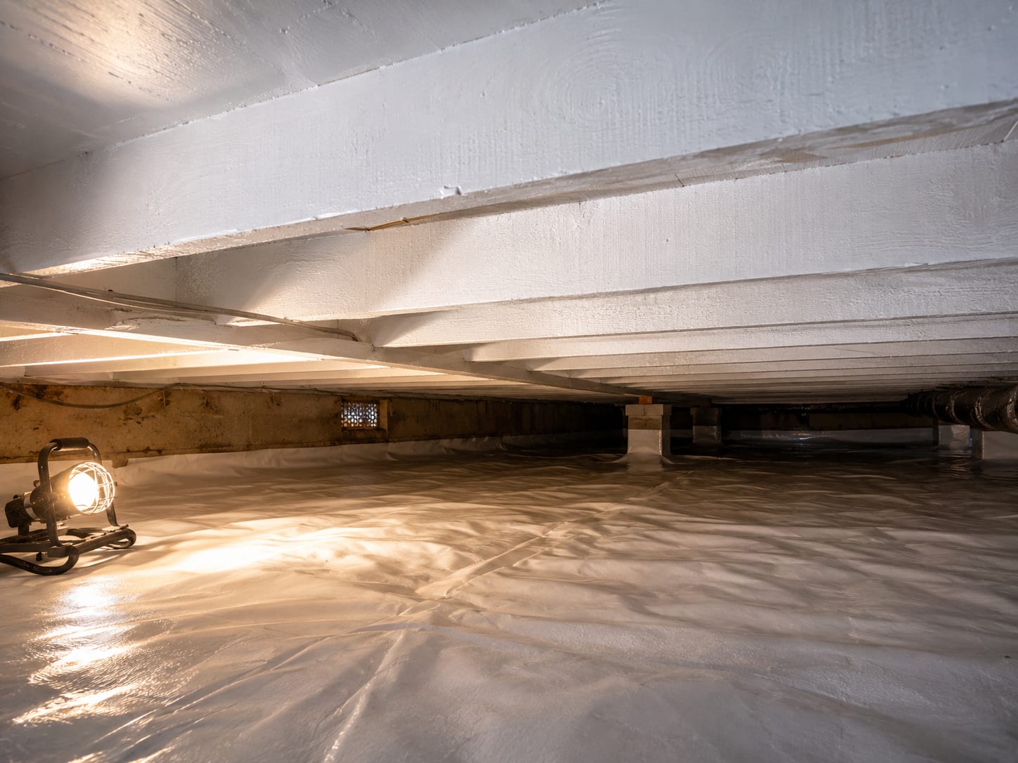 Clean bare wood floor joists and subfloor in a crawl space treated with white encapsulant coating visible under low framing