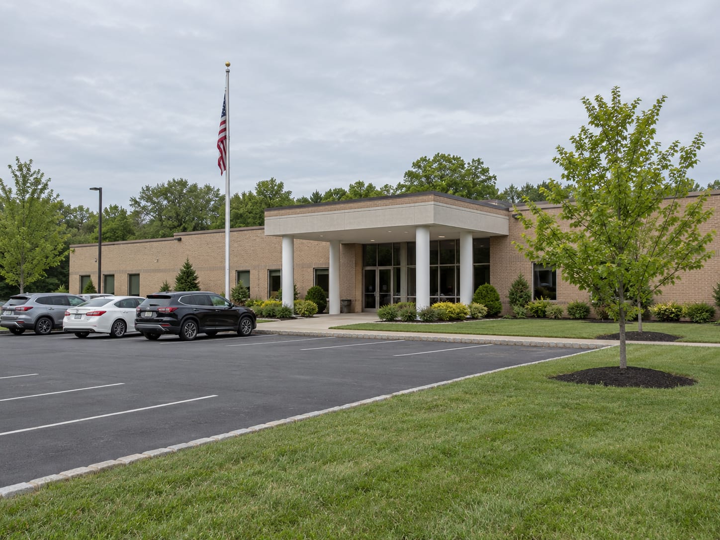 A low one storey brick municipal building with a flag pole, a paved parking lot and a mown lawn, in Monroe Township, New Jersey