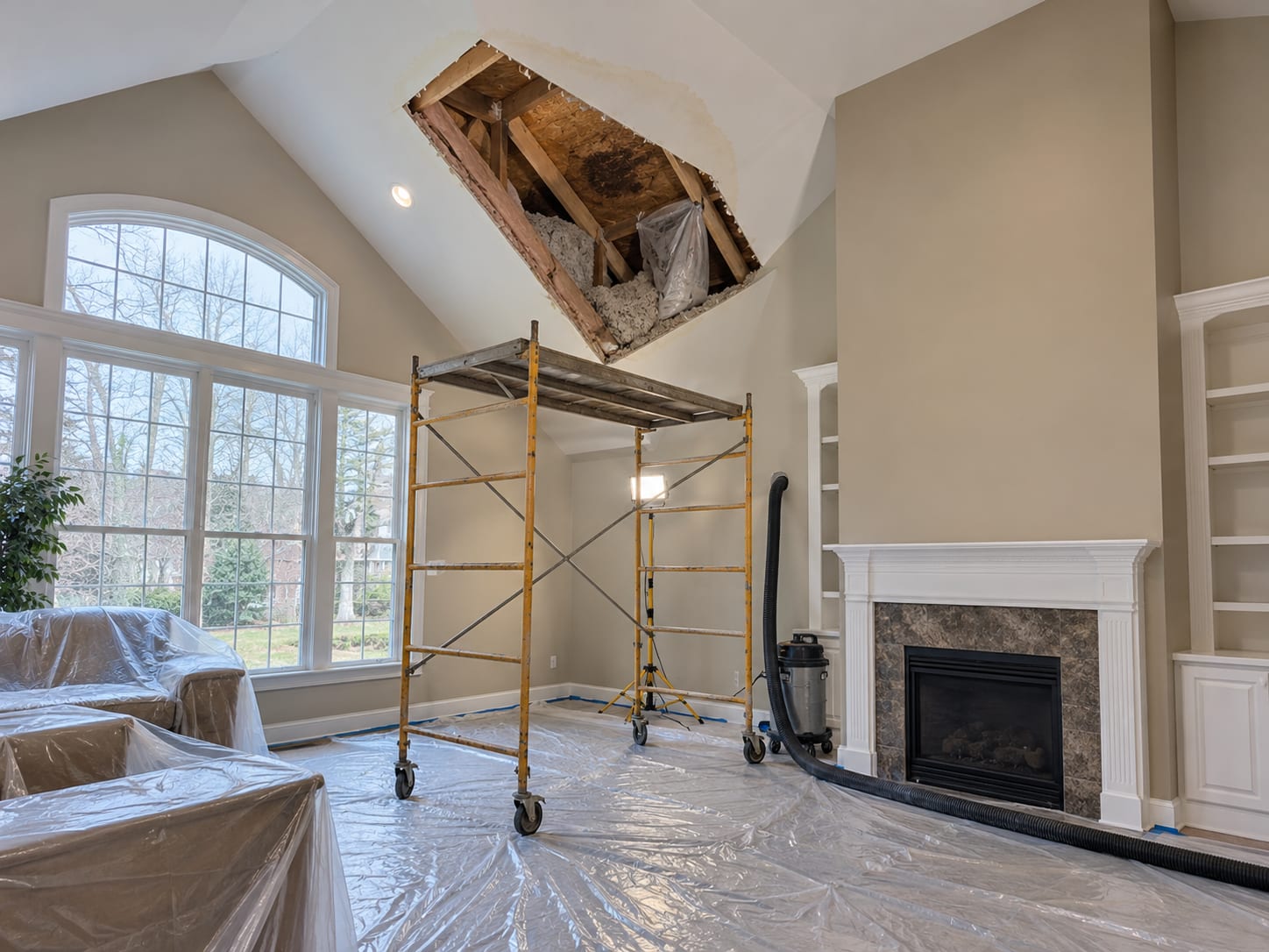 A vaulted great room ceiling with a section of drywall cut away beside a chimney chase, exposing wet insulation and stained rafters, in a Monroe Township, New Jersey home