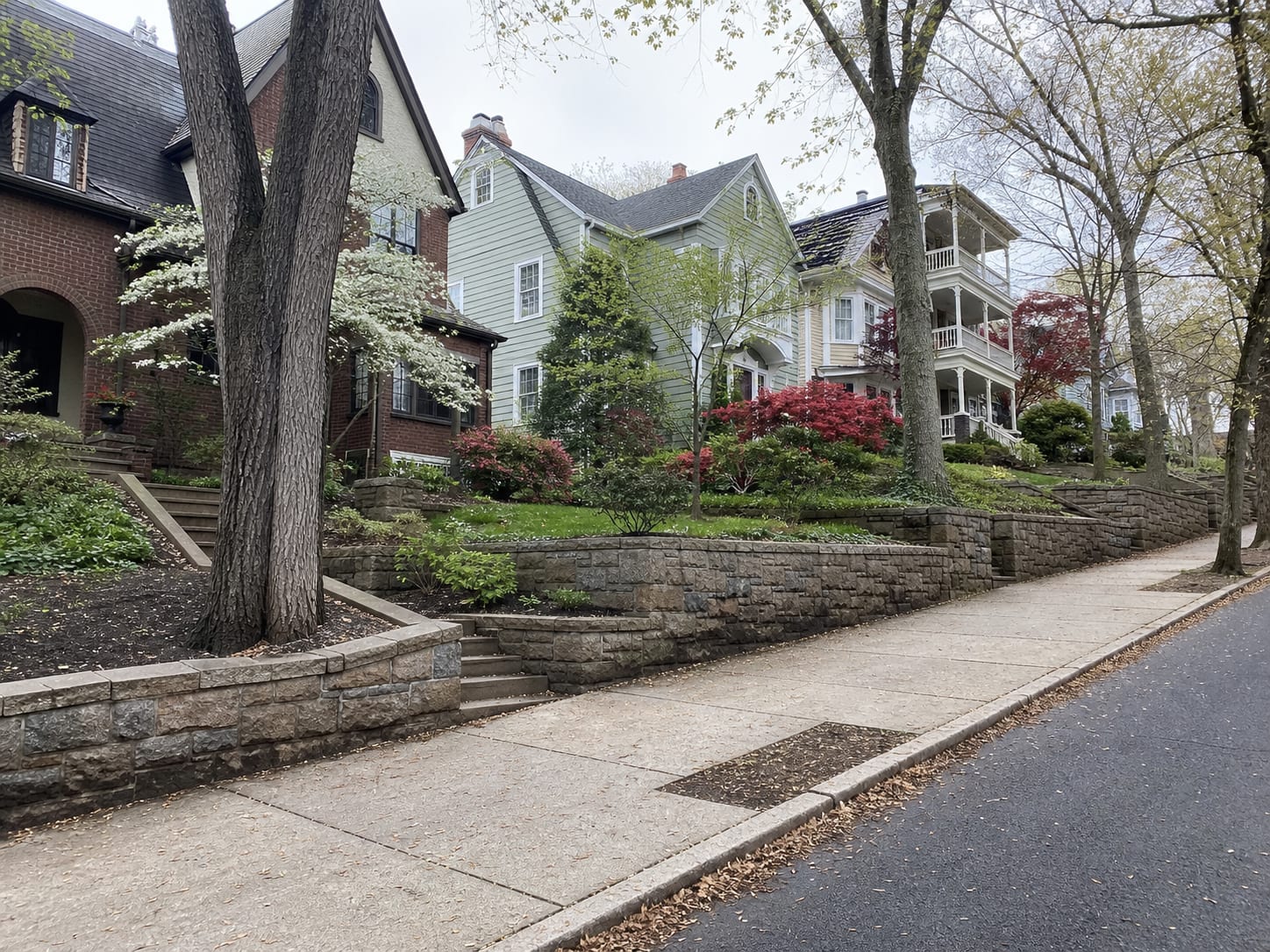 A residential street in Montclair, New Jersey climbing the grade, with stepped stone retaining walls at the sidewalk and mixed older houses standing well above street level