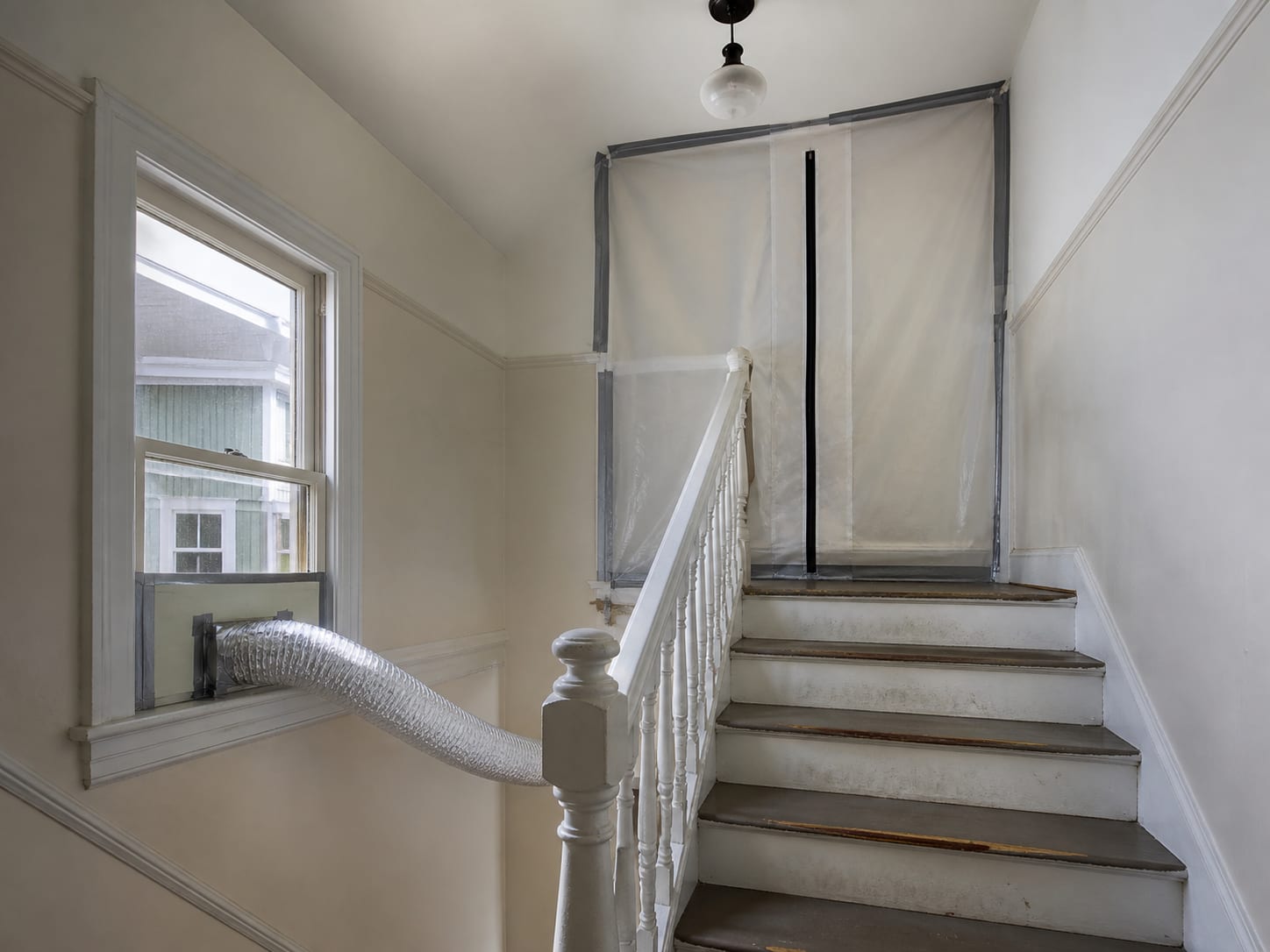 A zippered containment barrier sealed across a shared interior stair landing in a two family house in Montclair, New Jersey, with the stair continuing up past the barrier to the occupied unit