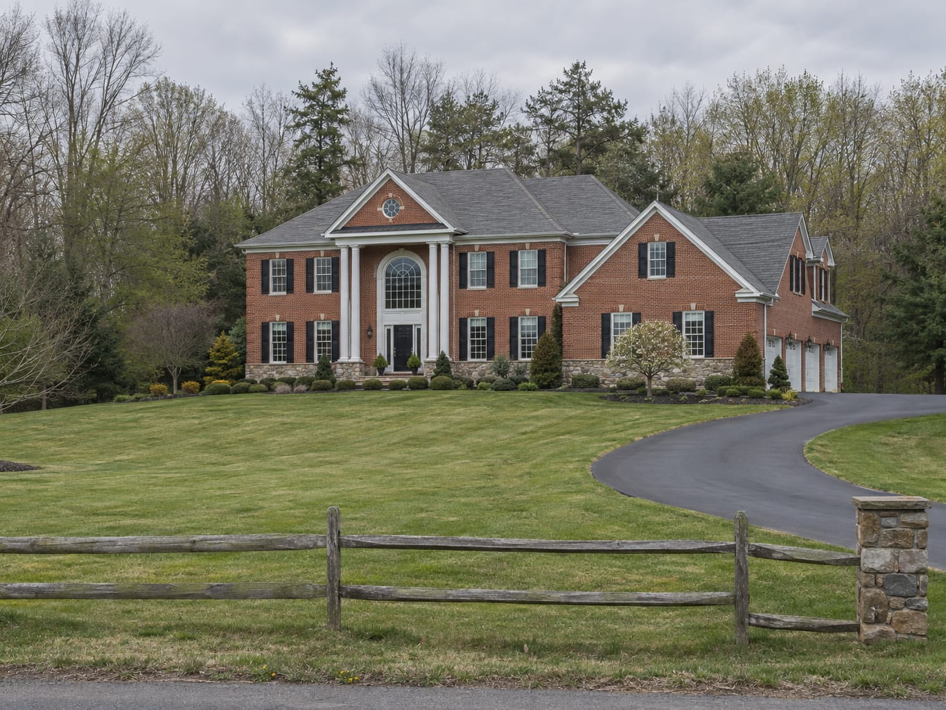 A large brick and stone fronted colonial with a side load garage on a wide lawn backed by woods, in Montgomery Township, New Jersey