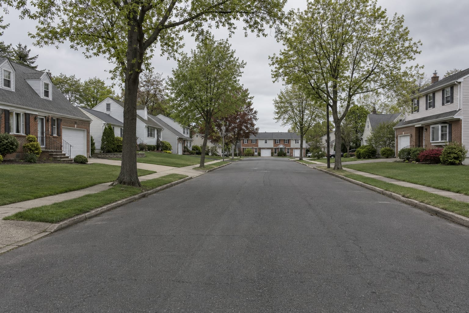 Cape Cod and split level houses in brick and siding on a straight suburban street, with a townhouse complex visible at the end, in North Brunswick, New Jersey