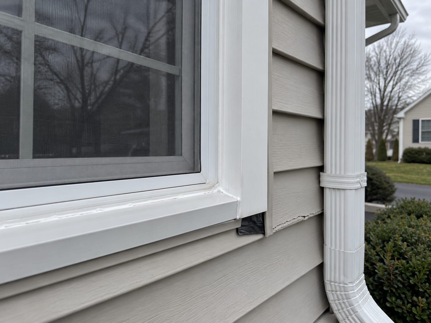The sill of a window on a vinyl sided house with a fresh bead of white caulk and a strip of new flashing tape under the trim, in North Brunswick, New Jersey