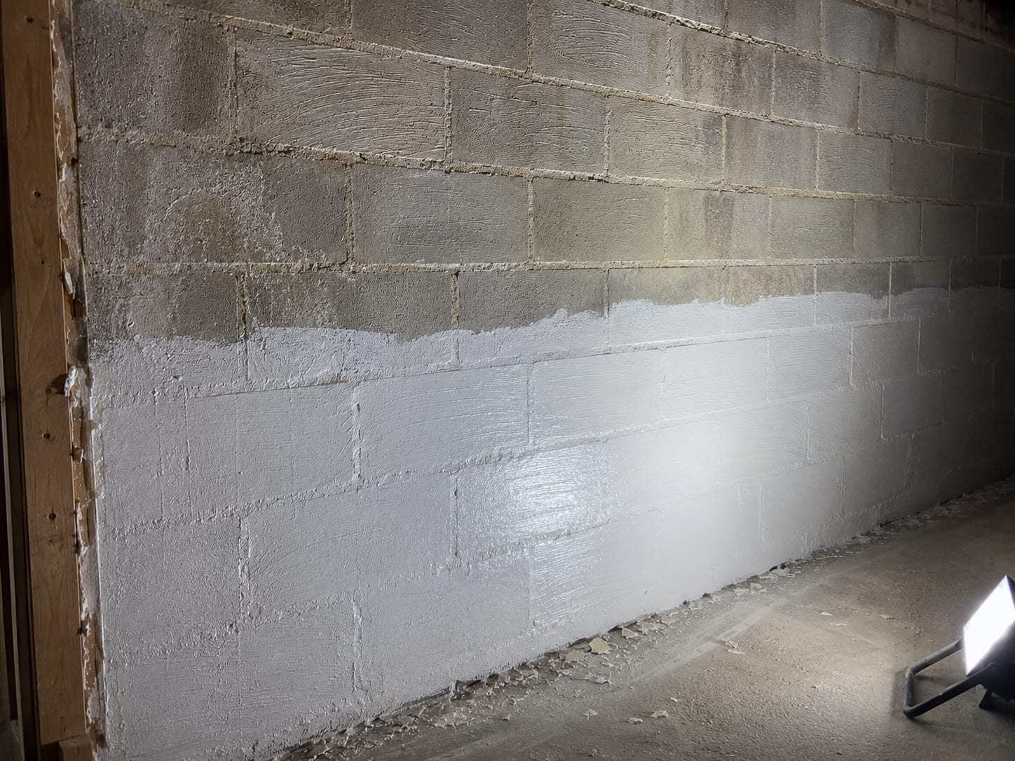 Close view of a remediated basement wall showing treated concrete block surface with residual cleaning marks and new encapsulant coating partially applied