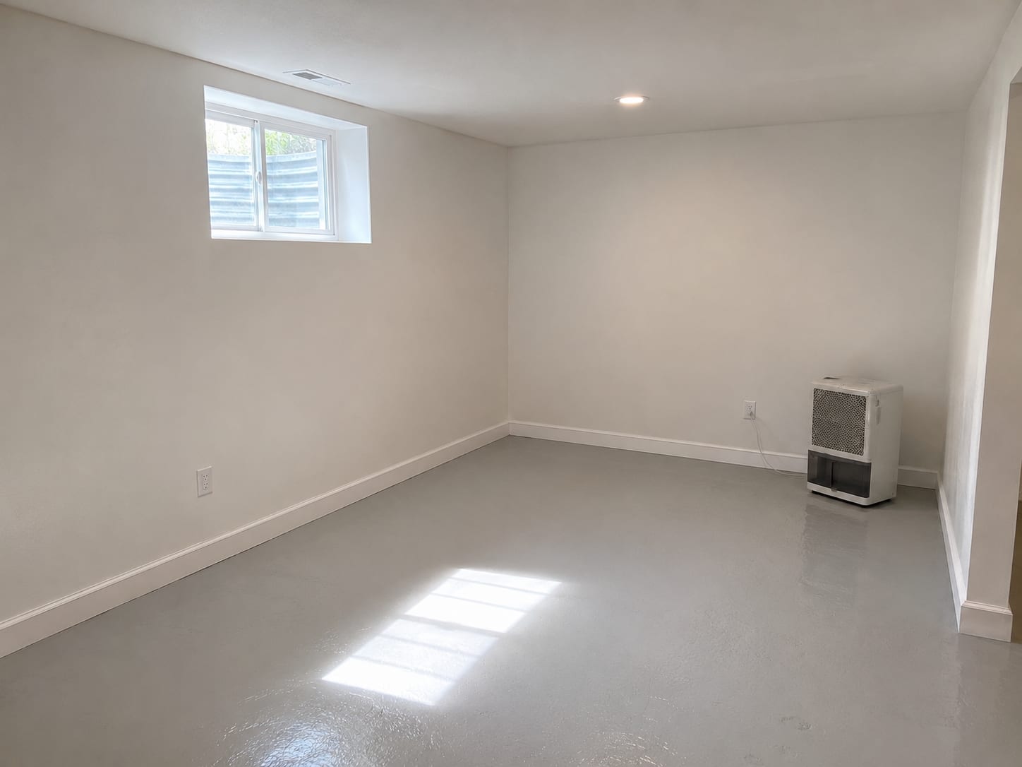 Clean finished basement room in a New Jersey home after completed mold remediation showing freshly painted drywall, new trim, and dehumidifier unit running in the corner