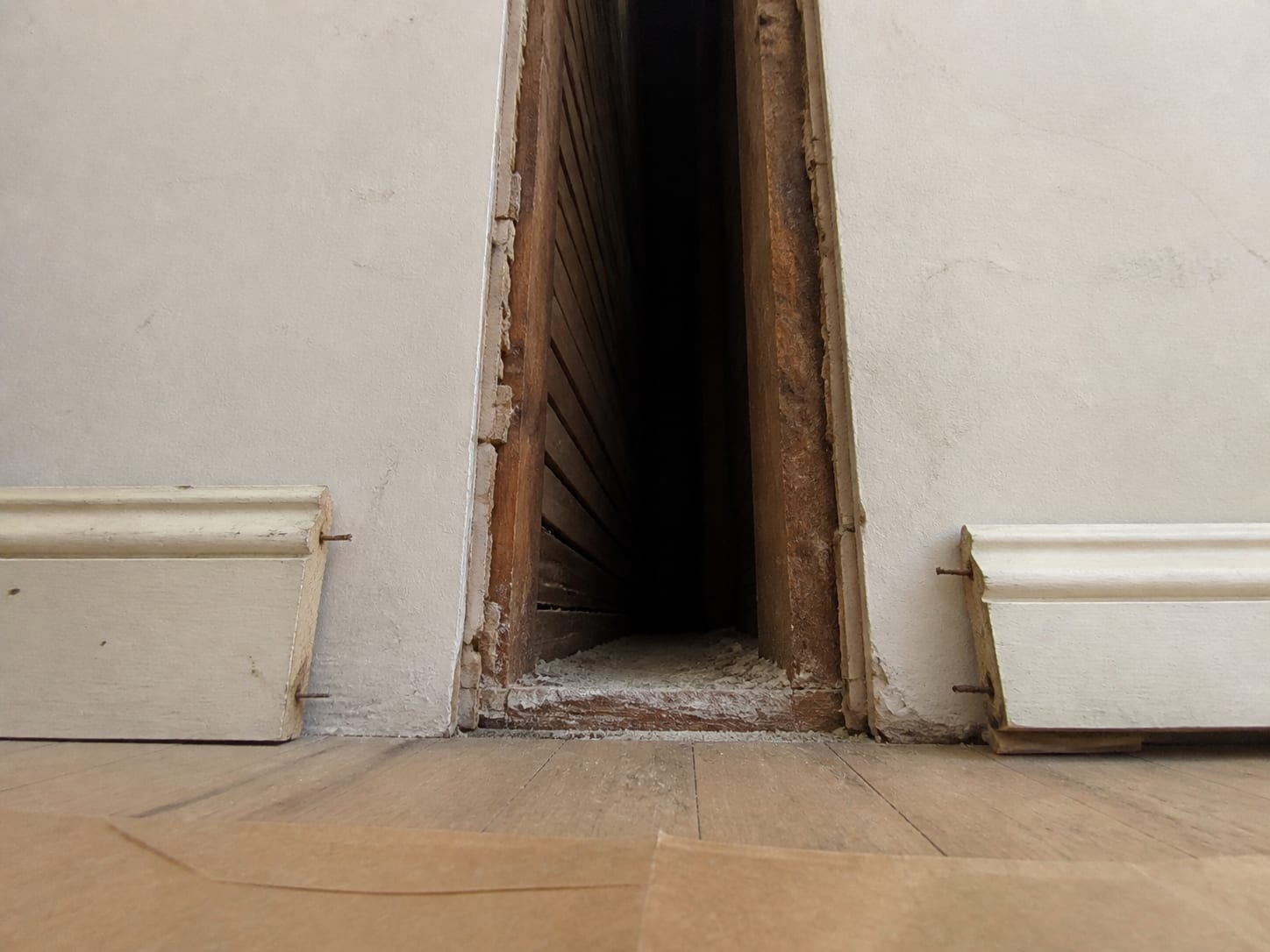 A low opening cut at the baseboard of an old frame wall in Ridgewood, New Jersey, looking up into a stud cavity that runs on uninterrupted past the floor line with no fire blocking