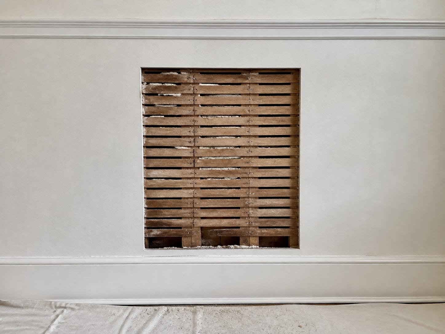 A neat rectangular opening cut in an old plaster wall in Short Hills, New Jersey, exposing horizontal wood lath and square cut studs while the surrounding plaster is left intact