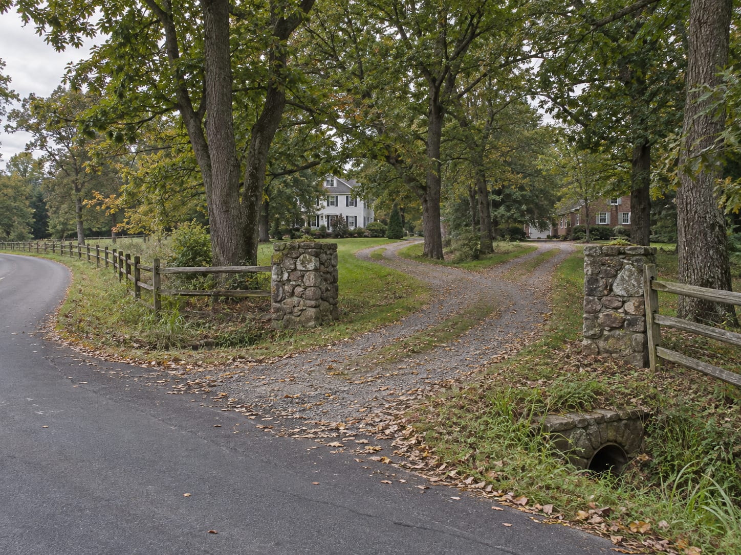 A narrow gravel driveway leading from a country road between fences and trees and forking to two houses, in Skillman, New Jersey
