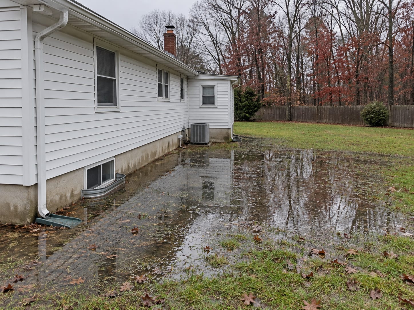 After heavy rain, standing water pools along the foundation of a South Brunswick ranch on a low, flat lot.