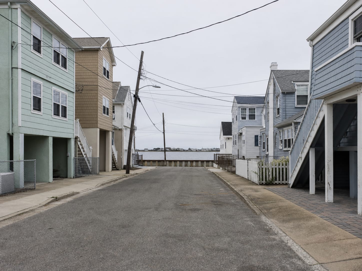 A back bay residential street in Wildwood, New Jersey of attached rows and older one and a half storey cottages, with overhead wires crossing and a boat slip at the far end